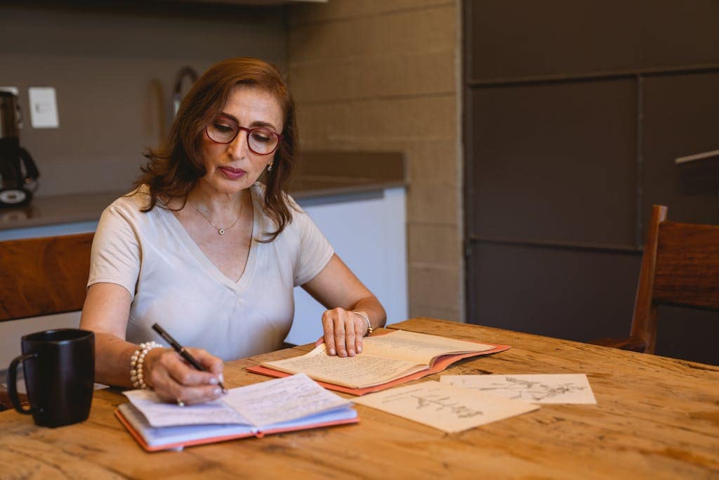 A woman writing notes with books and latte, thinking about new project