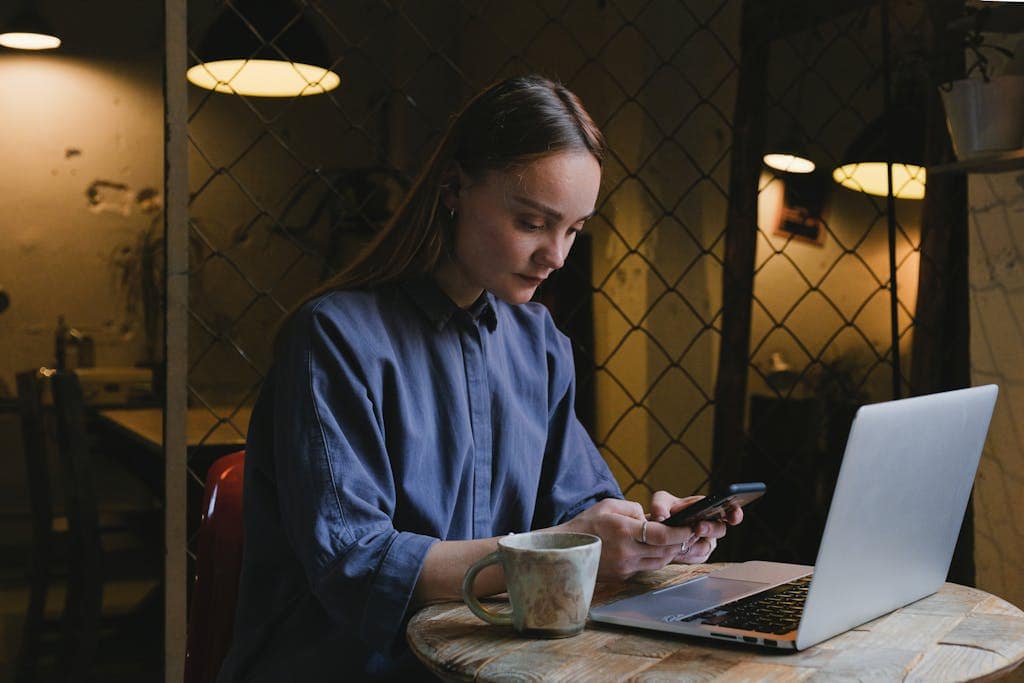 Woman concentrating on her work on a laptop and smartphone in a relaxed café setting.