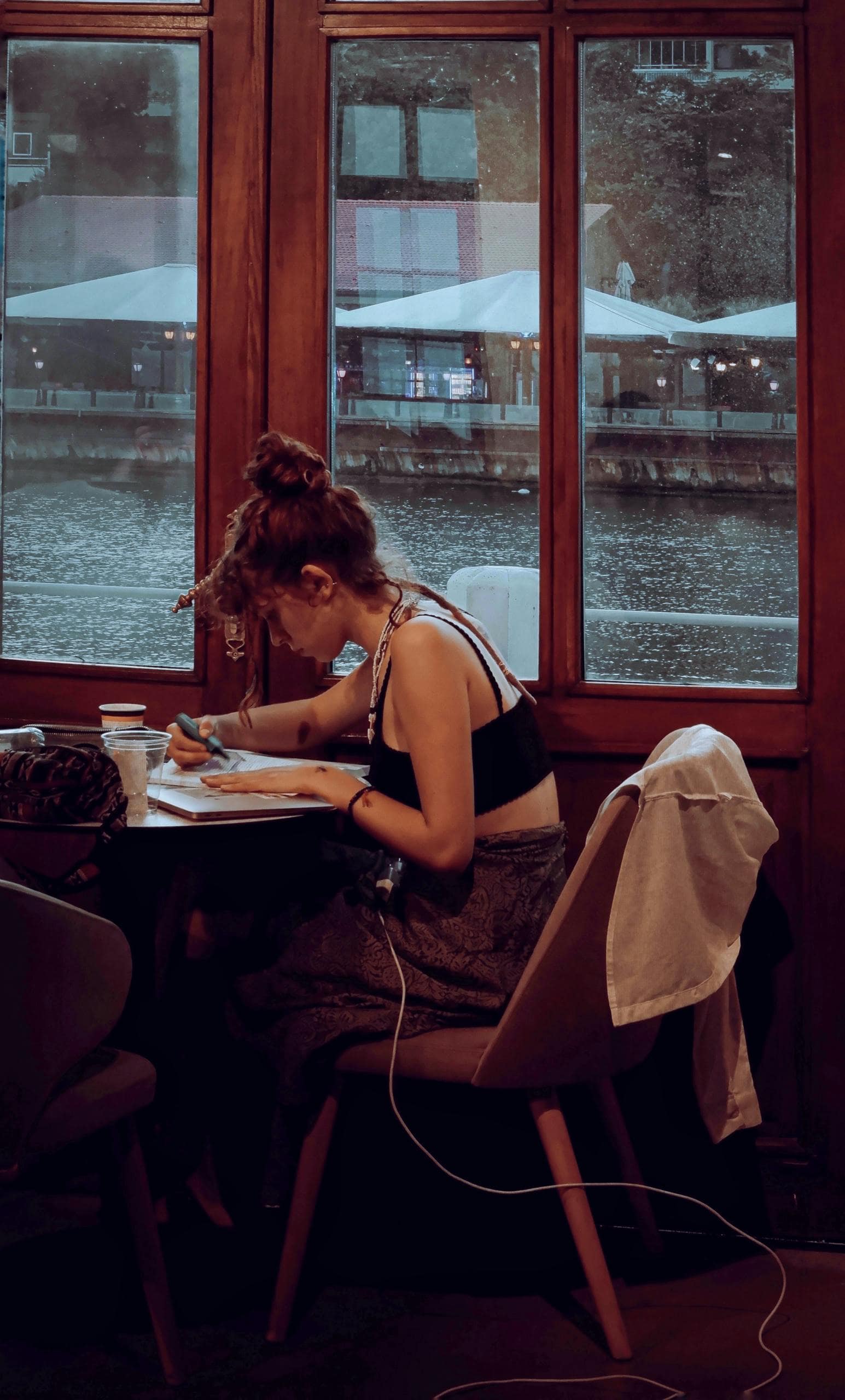 A young woman intensely studying at a café by the river, perfect for lifestyle or education themes.