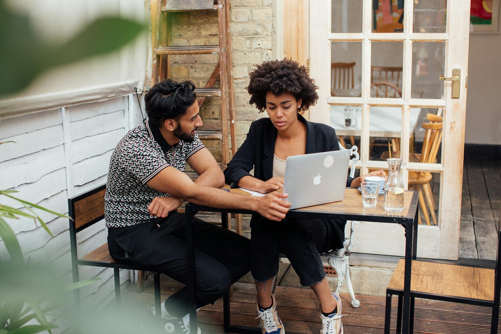A man and woman working together on a laptop at an outdoor terrace.