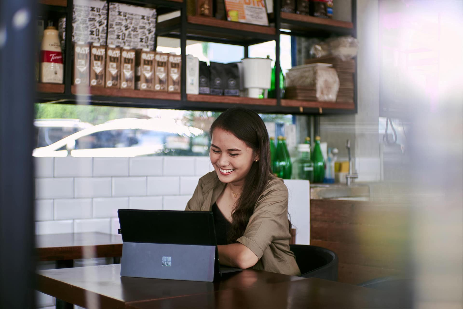 Smiling woman using laptop for remote work in a cozy cafe setting.