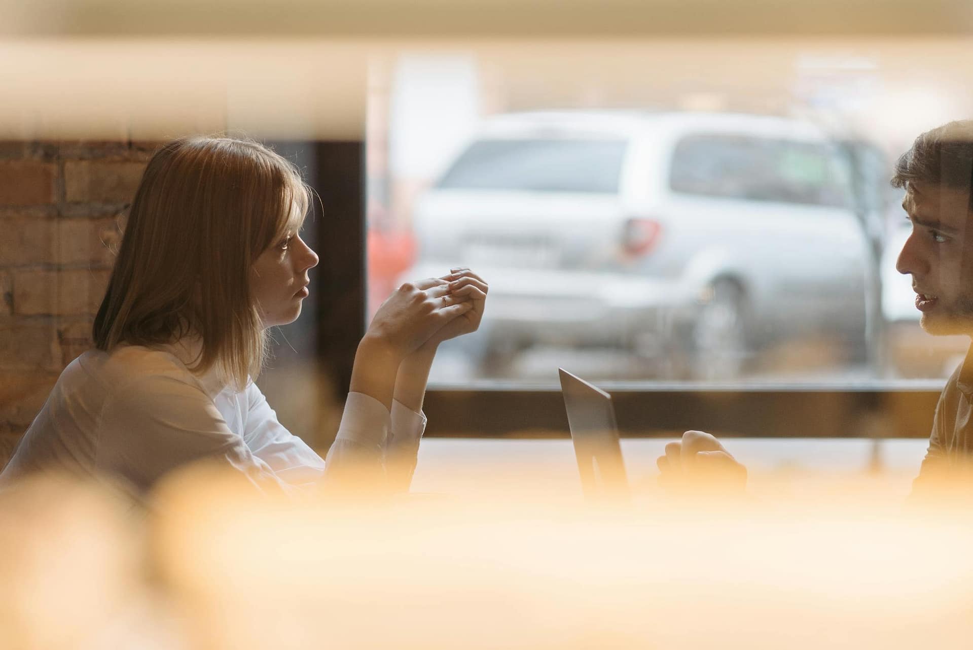 Two colleagues discuss ideas at a coffee shop table with a laptop.